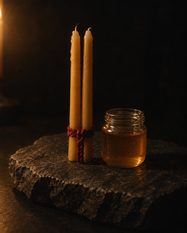 Two candles bound at the base with red cord beside an open jar of honey