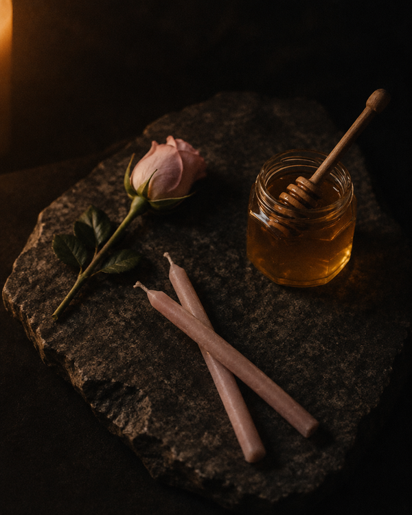 A pale pink rosebud, two unlit candles crossed at the base, and a jar of honey
