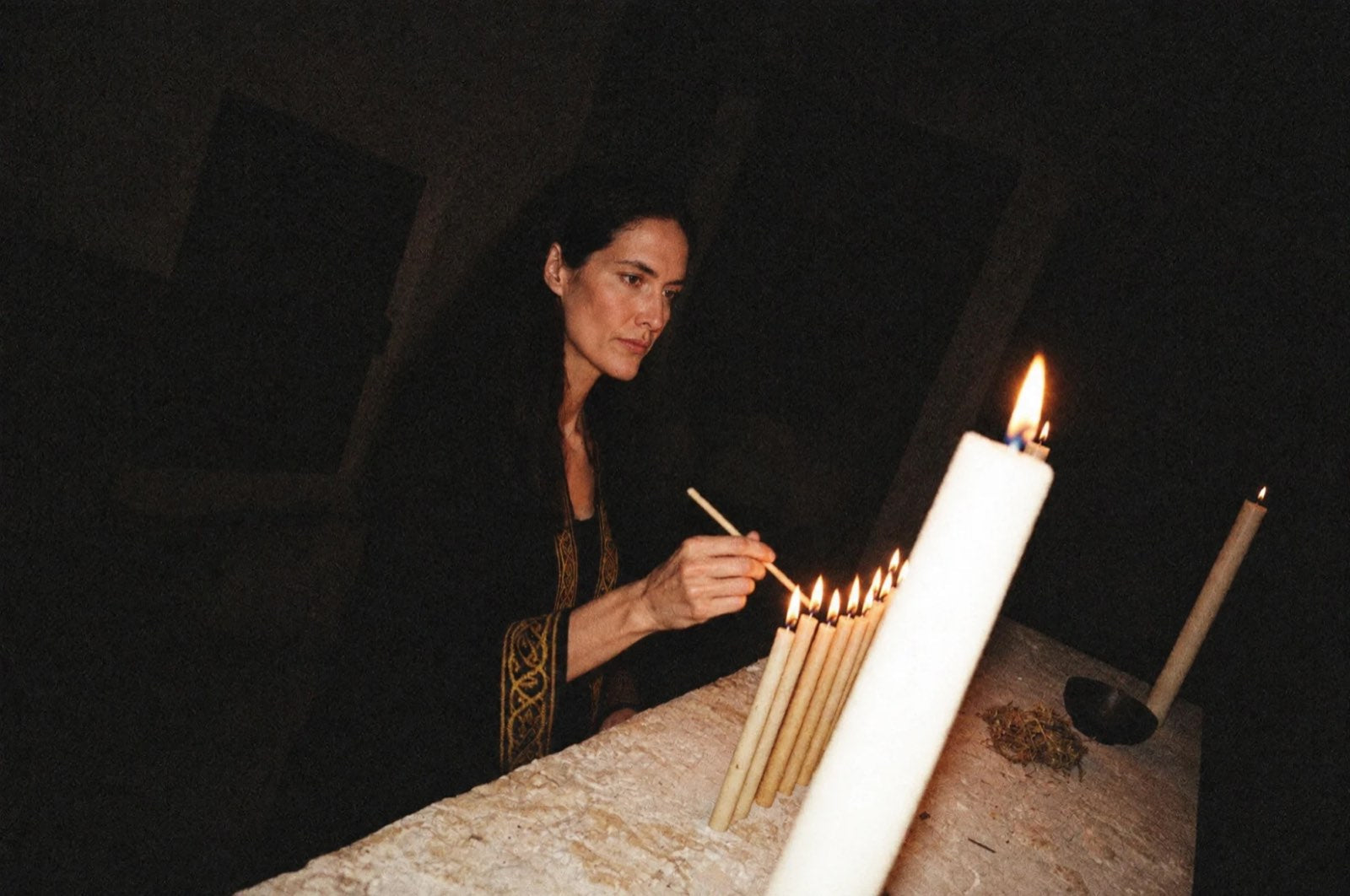 Amara lighting a row of beeswax tapers on her limestone altar
